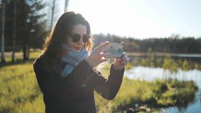 Young woman takes a photo with her phone with a view of the lake and walks away 