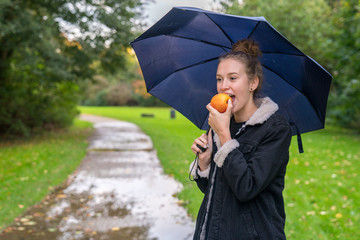 Eine junge Frau unter einem Regenschirm isst einen Apfel