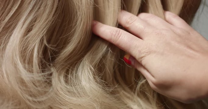 A woman's hand with bright manicure running through long wavy blond hair