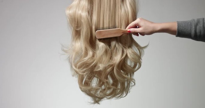 Brushing long wavy woman's blond hair with a hairbrush isolated on white