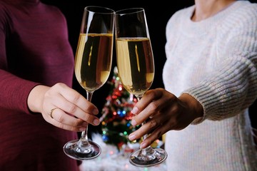 Christmas or New Year Celebration people hands with crystal glasses full of champagne near the Christmas tree and space for your text.