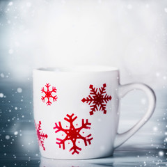 White mug with red snowflakes on blue snowfall background, front view. Happy winter holiday card layout