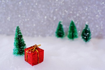 Christmas home decoration with Little handmade gift box in a snow covered miniature evergreen forest and bokeh light for copy space.