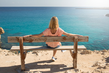A girl sits on a bench and looks at the sea, view from the back