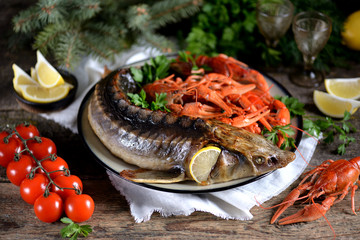 Baked whole sturgeon with boiled crawfish and lemon on an old wooden background. Rustic style.