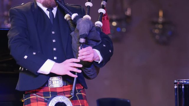 Bagpipe player in a kilt plays musical instrument at the stage