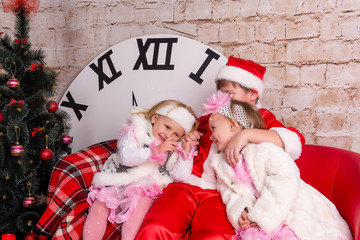 Obraz premium The children, a boy dressed as Santa Claus and two girls in white coats posing against the backdrop of the Christmas decorations in the studio.