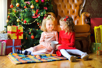 Fototapeta na wymiar girls sit on the floor near the festive Christmas tree and drink hot tea.