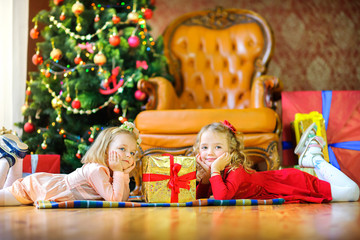 Fototapeta na wymiar two girls lie on the floor near the gifts and dream, in the background a festive Christmas tree.