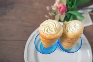 Two cream horns, pastry horn with white cream filling,  creamy cones in the blue glass on wooden table background.