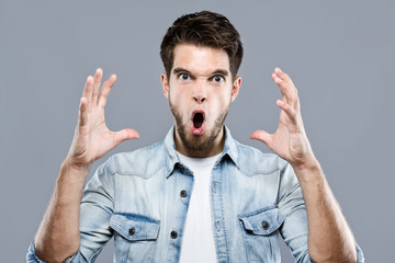 Angry young man screaming over gray background.