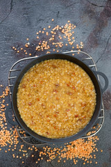 Cast-iron pan with indian red lentil soup, above view with space on a weathered asphalt background