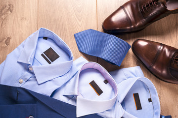 set of classic mens clothes - blue suit, shirts, brown shoes, belt and tie on wooden background.