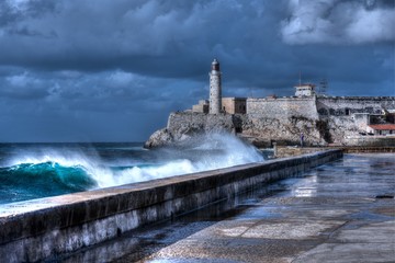 Cuba, Havana. Waves Breaking on the Malecon Sea Front. El Morro Fort in Background
