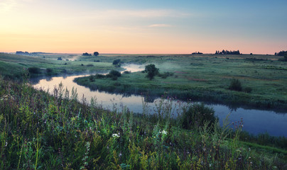 Foggy summer landscape with river.Green meadows at sunrise.