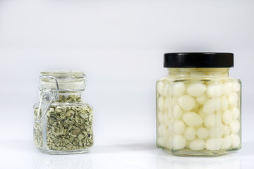 Tasty seasoned vegetables in jars. Kitchen pantry with mortar. White background,