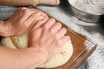 Female chef kneading dough on wooden board at kitchen