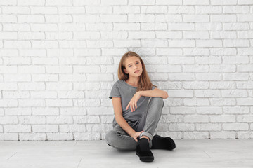 Little fashionable girl sitting on floor near brick wall