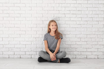 Little fashionable girl sitting on floor near brick wall