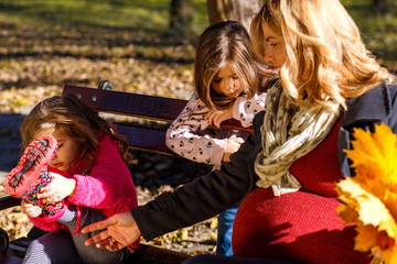Pregnant mother enjoying with her two daughters in park on sunny autumn day.