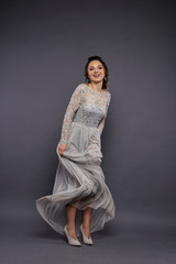 Studio Portrait of a Beautiful Bride Model in a Light Gray Wedding Dress with Elegant  Hairstyle and Pink Lips at Gray Background