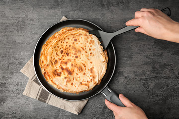 Woman holding pan with delicious thin pancakes on table