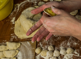 The hands of a woman cook cooked on a table of flour dough and make vareniki