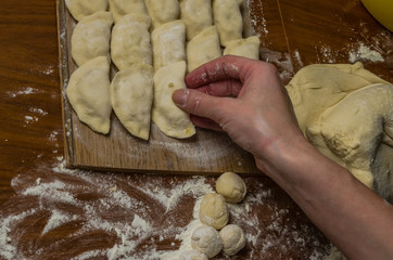 The hands of a woman cook cooked on a table of flour dough and make vareniki