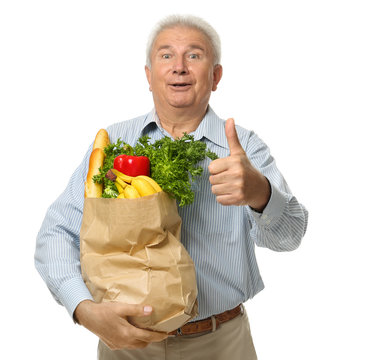 Elderly man holding paper bag with groceries on white background