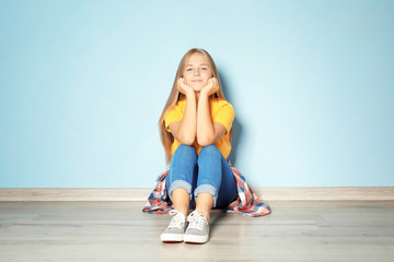 Fototapeta na wymiar Cute teenager girl sitting on floor near color wall