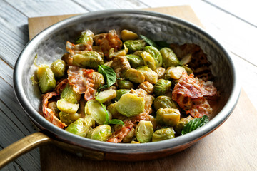 Frying pan with Brussels sprouts and bacon on table, closeup
