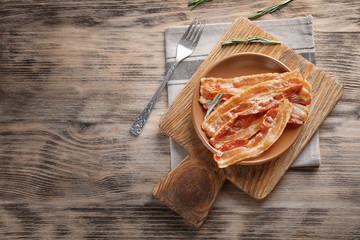 Board with plate of cooked bacon rashers on wooden table