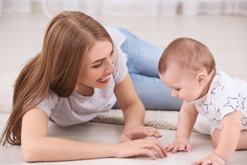 Young mother and cute baby playing on floor at home