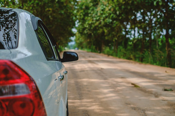 White car on rural road amidst green trees