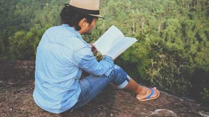 Asian man travel relax in the holiday. seats relax read books on rocky cliffs. On the Moutain. In Thailand