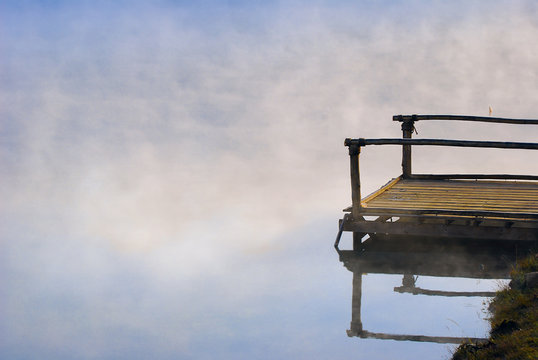Lonely wooden deck pier among the fog in the river of eary morning sunshine.