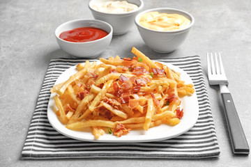 Plate with french fries and bacon on table