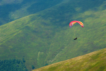 Paraglider flies over a mountain valley on a sunny summer day. Paragliding in the Carpathians in the summer.