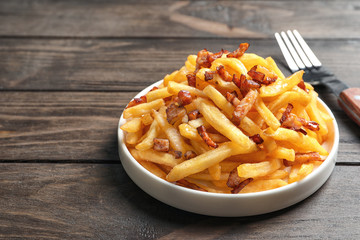 Plate with french fries and bacon on wooden background