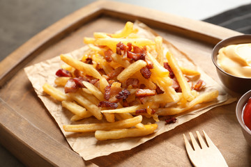 Wooden board with french fries and bacon on table