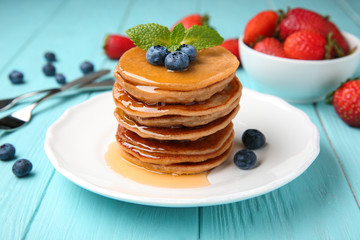 Plate with buckwheat pancakes, honey and berries on wooden table