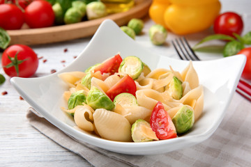 Plate of pasta with Brussels sprouts and tomatoes on table