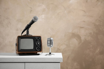 Retro portable TV and microphones on table against light wall