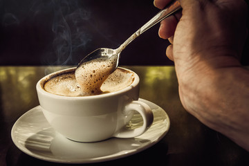 A woman holding coffee spoon to stir hot coffee on wooden table