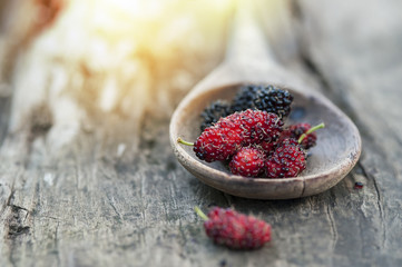 Mulberry red and black berry fruit in wooden spoon locates on a surface vintage wooden background