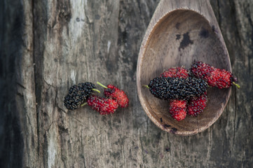Mulberry red and black berry fruit in wooden spoon locates on a surface vintage wooden background