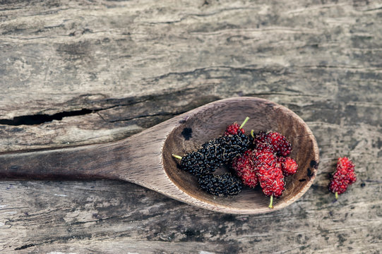 Mulberry red and black berry fruit in wooden spoon locates on a surface vintage wooden background