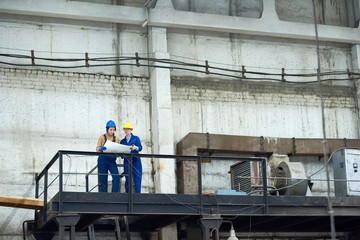 Busy confident female factory workers analyzing blueprint while working in old factory and standing...