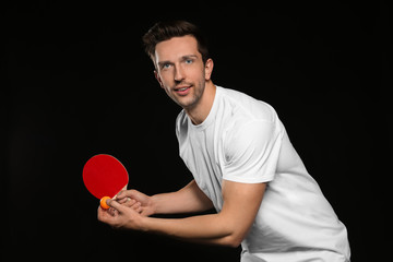 Young man with tennis racket and ball on dark background