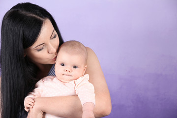 Young mother and cute baby on color background